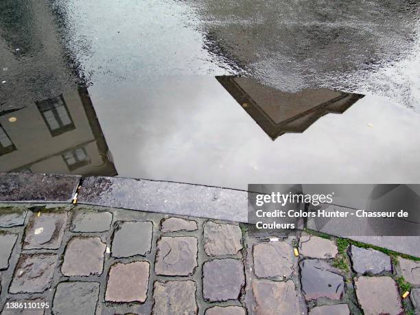 buildings are reflected in a puddle at the edge of a sidewalk in brussels - rain gutter imagens e fotografias de stock