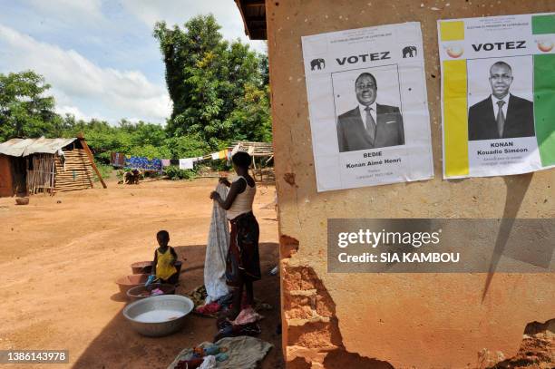 Woman washes clothes in Amichiakro in a cocoa plantation in Divo on October 25, 2010 as posters portraying Ivory Coast's presidential candidates,...