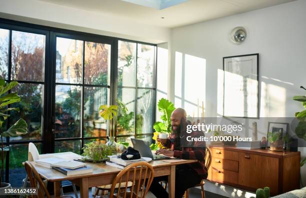 black entrepreneur drinking coffee and having relaxed work meeting on laptop in home office - freelance work candid stock pictures, royalty-free photos & images