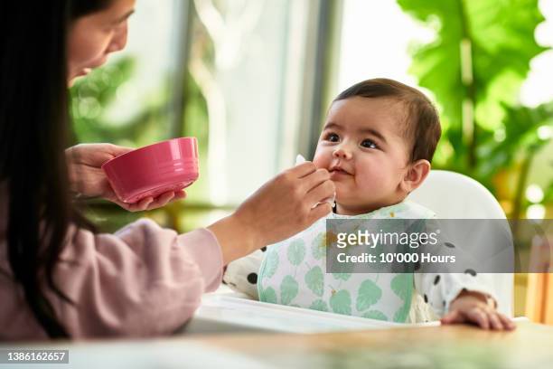 mature chinese mother spoon feeding cheerful baby daughter - asian baby eating fotografías e imágenes de stock