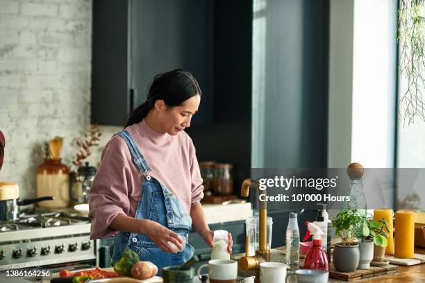 mature chinese woman standing at kitchen sink preparing bottle for baby - stereotypical homemaker stock pictures, royalty-free photos & images