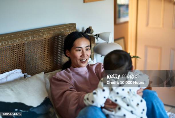 proud mature mother playing with baby daughter on bed and smiling - mature asian woman candid foto e immagini stock