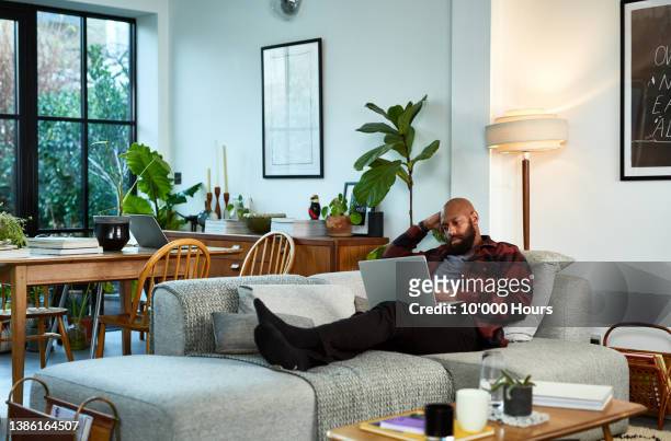 black man in his 30s lying on sofa with feet up, using laptop - s thirtysomething stock pictures, royalty-free photos & images