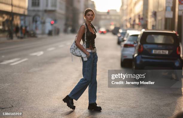 Celine Bethmann wearing gold jewelry, a black crop leather top, a Balenciaga white Le Cagole big leather bag, a white belt, blue jeans and Prada...