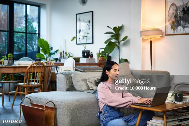 mature chinese woman sitting on living room floor home using laptop, working from home - frau am laptop stock-fotos und bilder