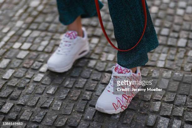 Palina Kozyrava wearing blue wide shiny pants and Skechers colorful heart sneaker on March 16, 2022 in Berlin, Germany.
