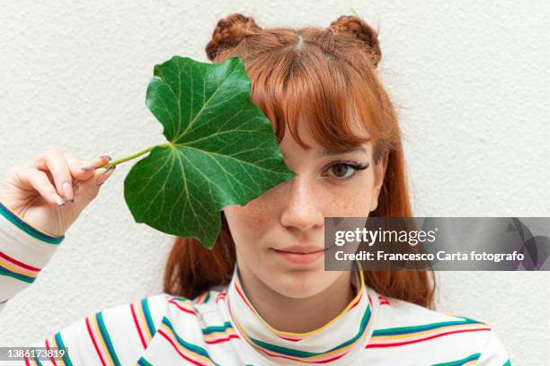 woman with orange hair covers one eye with an ivy leaf - oranje haar stockfoto's en -beelden