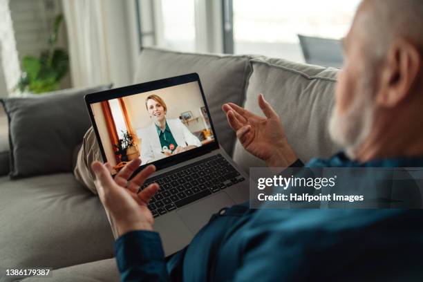 senior man sitting on sofa and having video call with his doctor. - telemedicine foto e immagini stock