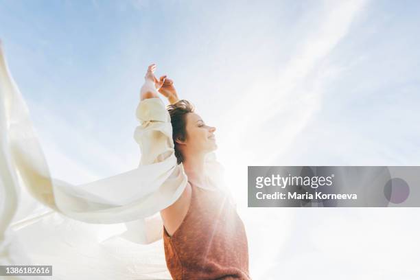 dreamy portrait of a young woman against the blue sky. - arms raised stock-fotos und bilder