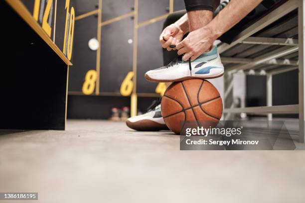 crop basketball player tying shoelaces in locker room - basketball shoe fotografías e imágenes de stock