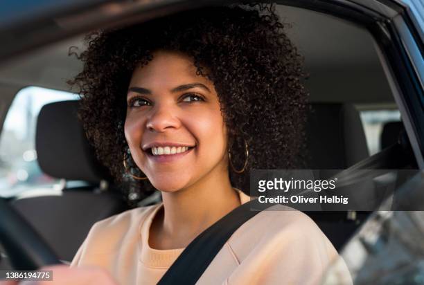 smiling woman driving, looking out a car window. happy woman holding a steering wheel in the vehicle. - woman driving stockfoto's en -beelden