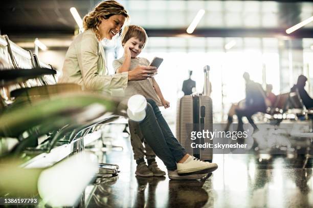 madre single e figlio che usano il telefono cellulare durante l'attesa del loro trasporto nell'area di partenza. - travel foto e immagini stock