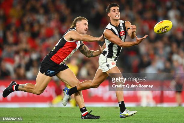 Nick Daicos of the Magpies handballs whilst being tackled by Dean Kent of the Saints during the round one AFL match between the St Kilda Saints and...