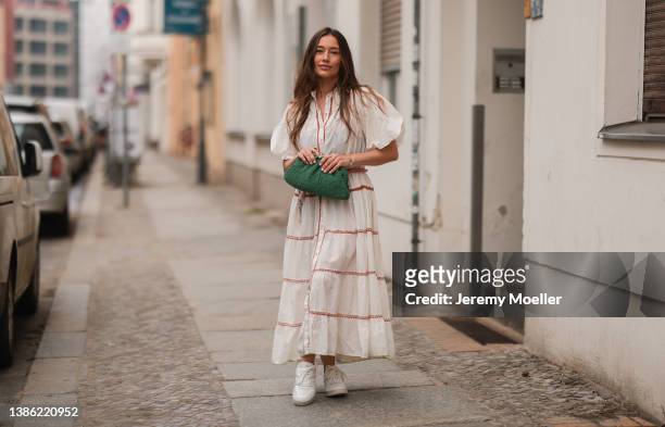 Anna Schürrle is wearing a white and red long dress with puffer-sleeves, white Celine sneaker and a green Clutch on March 17, 2022 in Berlin, Germany.