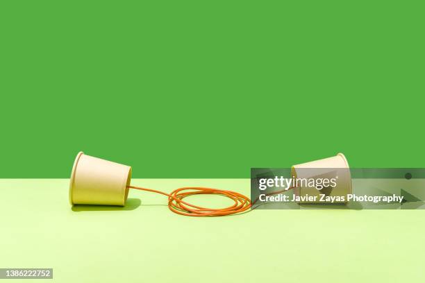 two paper cups united with an orange string on a green background - phone still life stock pictures, royalty-free photos & images