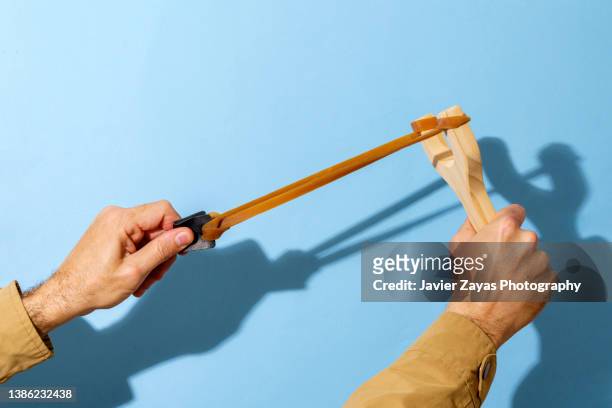 man shooting a slingshot on blue background - slingers stockfoto's en -beelden