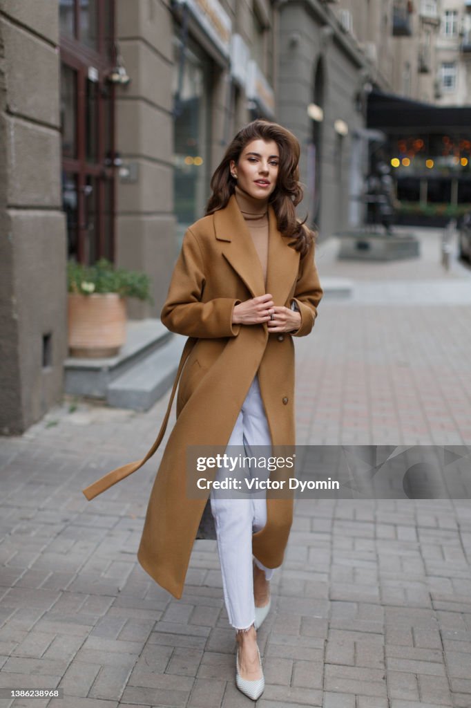 Young model with long hair in light brown coat goes towards the camera.