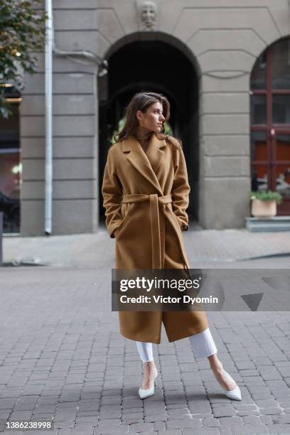 stylish girl stands in a light brown coat and white shoes looks away from the camera - a fall from grace 個照片及圖片檔