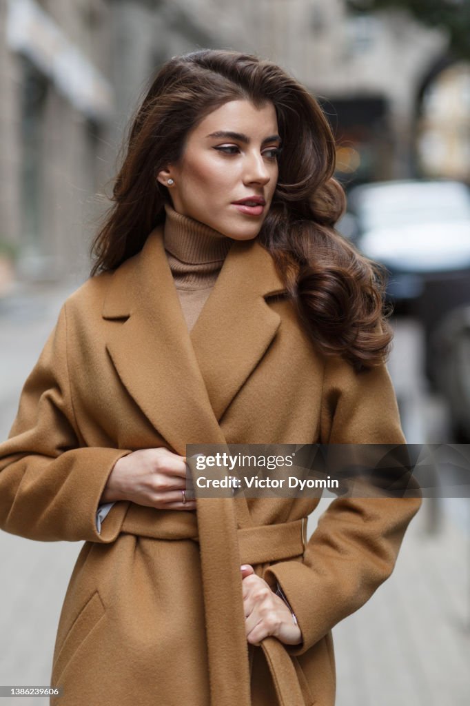 Portrait of beautiful lady in light brown coat tying her belt.