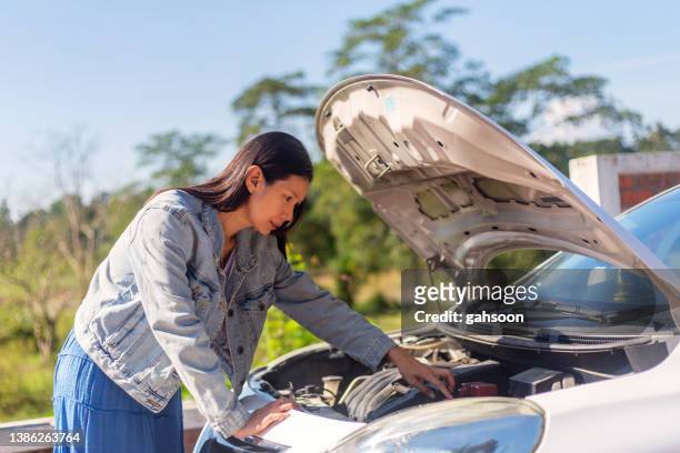 young asian woman looks under the hood of a broken car. - overheated stock pictures, royalty-free photos & images