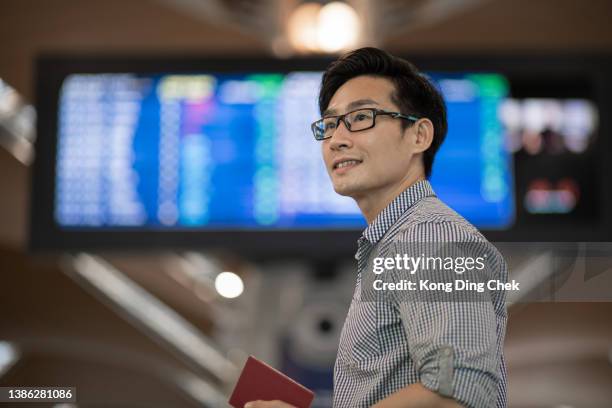 asian chinese man  checking boarding time in airport.  waiting in front arrival departure board. - airport terminal stock pictures, royalty-free photos & images