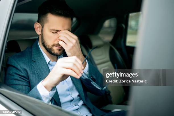 tired businessman with eyeglasses sitting on backseat of limousine with eyes closed - holding nose stock pictures, royalty-free photos & images