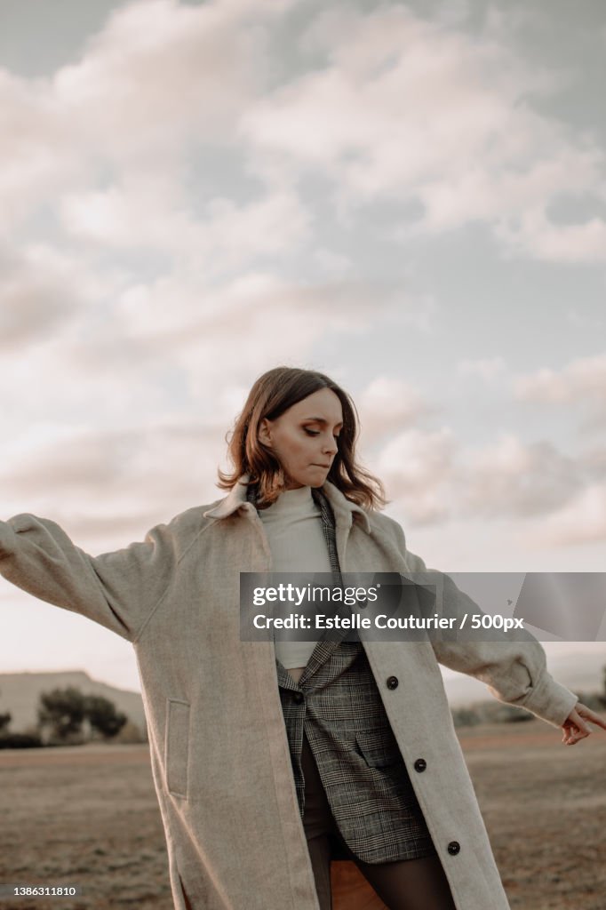 Young woman in warm clothing looking away while In the meadow at sunrise standing against sky,France