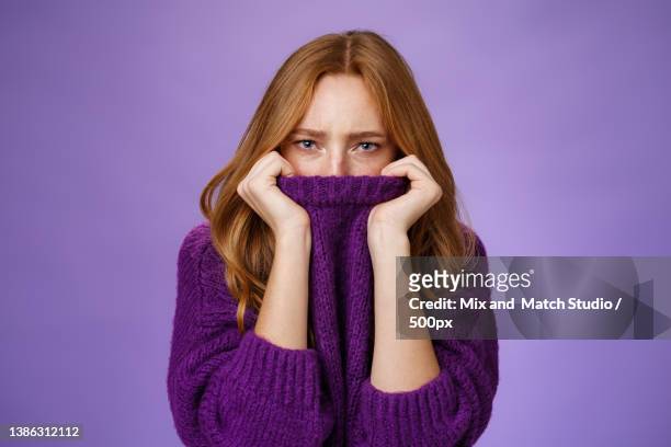 gloomy upset redhead girlfriend pulling collar of purple sweater on - foxy lady stock-fotos und bilder