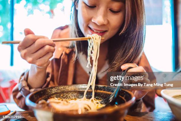 young pretty asian woman enjoying japanese noodle soup in a japanese restaurant - japanische küche stock-fotos und bilder