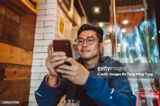 young handsome asian man making order from the digital menu on smartphone in restaurant - contact opnemen stockfoto's en -beelden