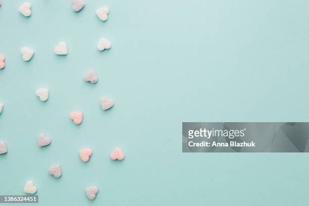 multi-colored pink and white candies in heart shape over pastel blue background - candy hearts stock pictures, royalty-free photos & images