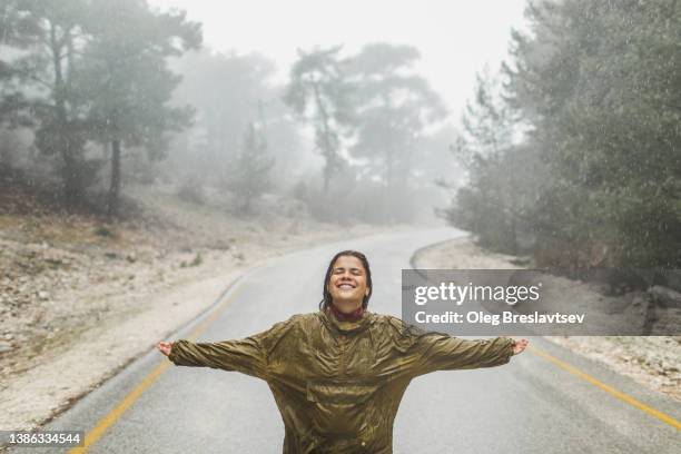 happy woman laughing in raincoat under heavy rain - regen stock-fotos und bilder