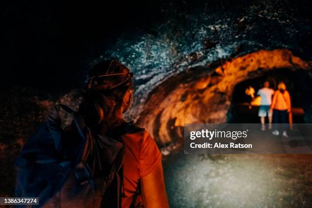 a woman wearing a headlamp walks through a long underground lava tube in hawaii - lava tube stock pictures, royalty-free photos & images