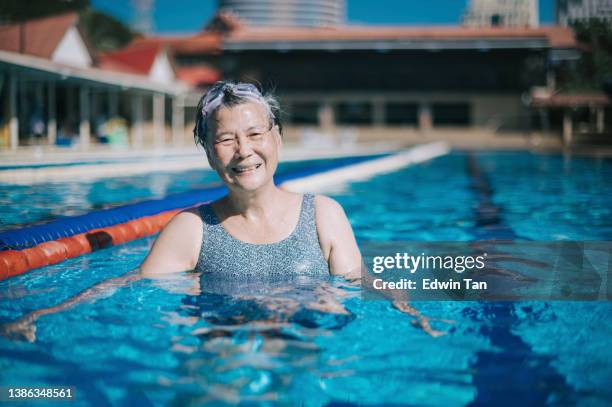 asian chinese senior woman looking at camera smiling in swimming pool during weekend morning - chinese people swimming stock pictures, royalty-free photos & images