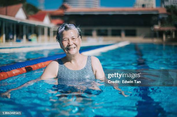 asian chinese senior woman looking at camera smiling in swimming pool during weekend morning - bath relaxation stock pictures, royalty-free photos & images