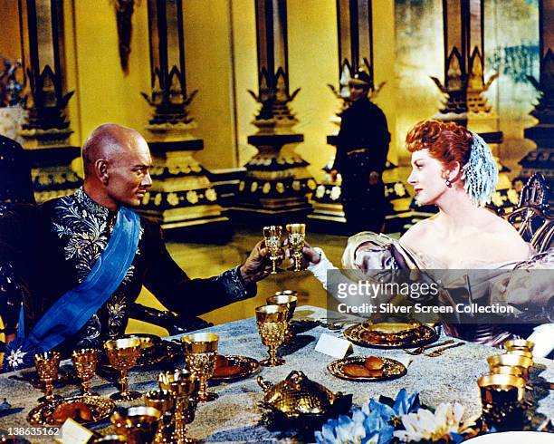 Yul Brynner , Russian-born US actor, and Deborah Kerr , both in costume, seated at a dining table in a publicity still issued for the film, 'The King...