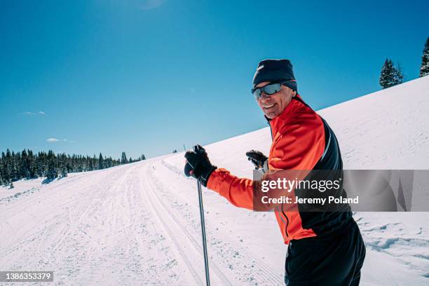 close-up medium portrait of a cheerful cross-country skier looking back at camera while skiing along a groomed trail on a clear, sunny day in the grand mesa national forest in colorado with copy space - sunny winter stock pictures, royalty-free photos & images