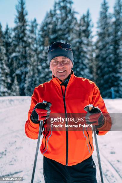 close-up portrait of a cheerful cross-country skier standing and holding his ski poles looking at the camera on a groomed trail on a clear, sunny day in colorado - ski poles stock pictures, royalty-free photos & images