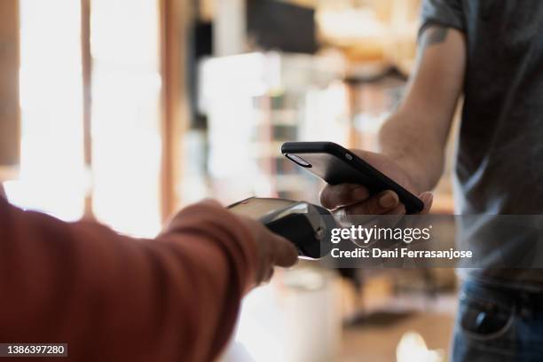 close-up shot of hand holding a cellular phone paying a bill at a datafono - communication en champ proche photos et images de collection