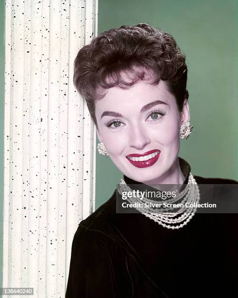 Ann Blyth, US actress, wearing a black jumper with a pearl necklace and matching earrings in a studio portrait, against a green background, circa...