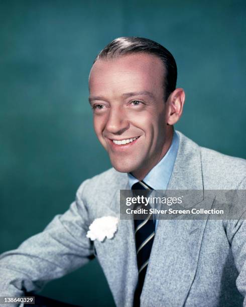 Fred Astaire , US actor and dancer, wearing a light blue shirt, black and white striped tie, and a grey jacket, smiling in a studio portrait, against...