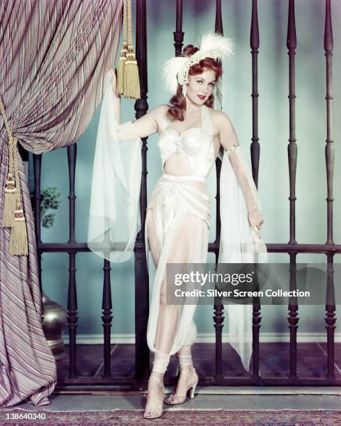 Rhonda Fleming, US actress, wearing a white sheer outfit, with white feathers in her hair, in a studio portrait, circa 1955.