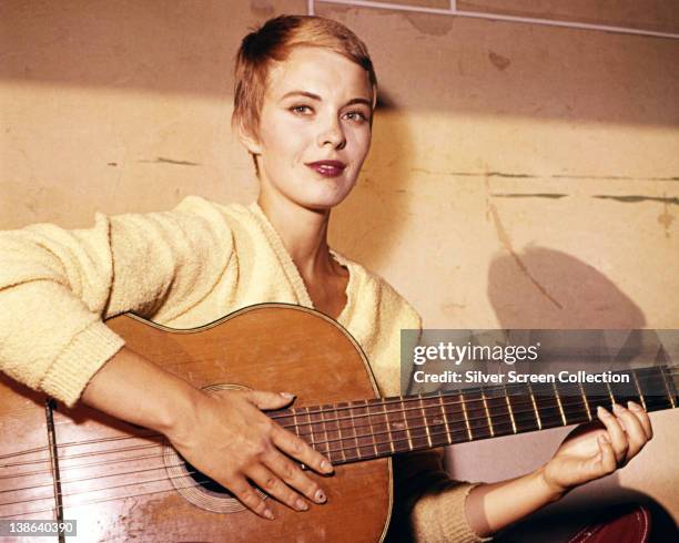 Jean Seberg , US actress, wearing a yellow jumper as she plays an acoustic guitar, circa 1970.