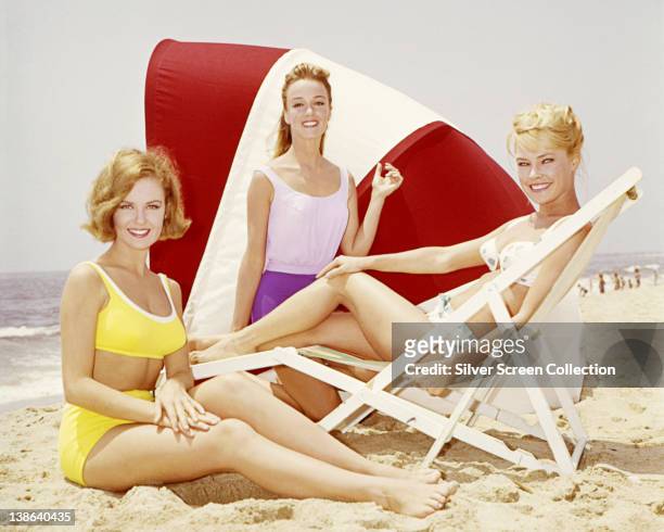 Shelley Fabares, US actress and singer, wearing a yellow bikini, alongside two women in beachwear, posing on a beach, circa 1965.
