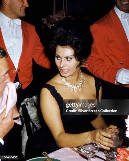 Sophia Loren, Italian actress, wearing a sleeveless black dress with a diamond necklace as she turns to speak to the person beside her, circa 1960.