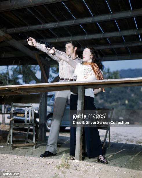 Audie Murphy , US actor, aiming a handgun on a firing range, alongside his wife, Wanda Hendrix , who holds a similar pose, USA, 1955.