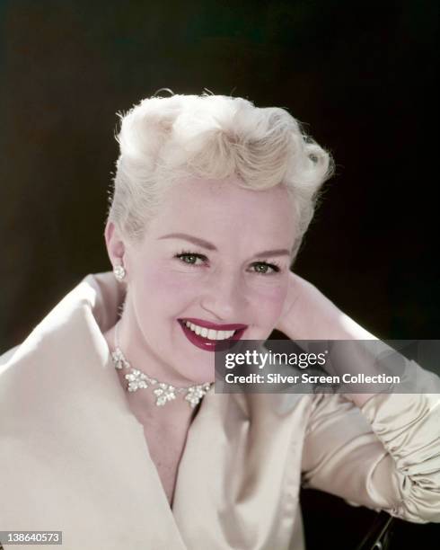 Betty Grable , US actress, dancer and singer, wearing a white jacket, with a floral motif choker around her neck, in a studio portrait, against a...