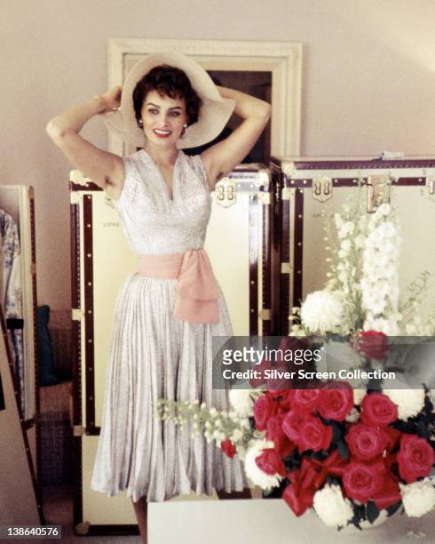Sophia Loren, Italian actress, wearing a white sleeveless dress, with a pink sash around the waist, posing with a floppy-brimmed hat on her head,...