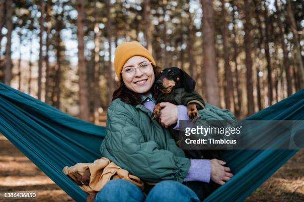 beautiful young adult woman with her dog sitting on hammock in forest - teal portrait stockfoto's en -beelden