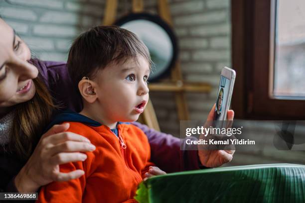 mother helping her son who is wearing a hearing aid. - homeschooling stock pictures, royalty-free photos & images